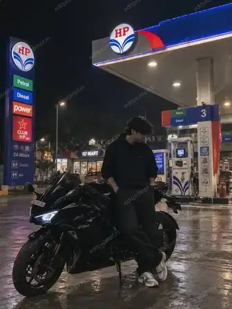 Bike petrol pump photo prompt for boys — boy in a black hoodie leaning on a black sports bike at a lit petrol pump at night